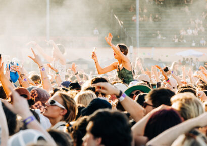 Girl with arms up on someone's shoulders in a busy music festival crowd.